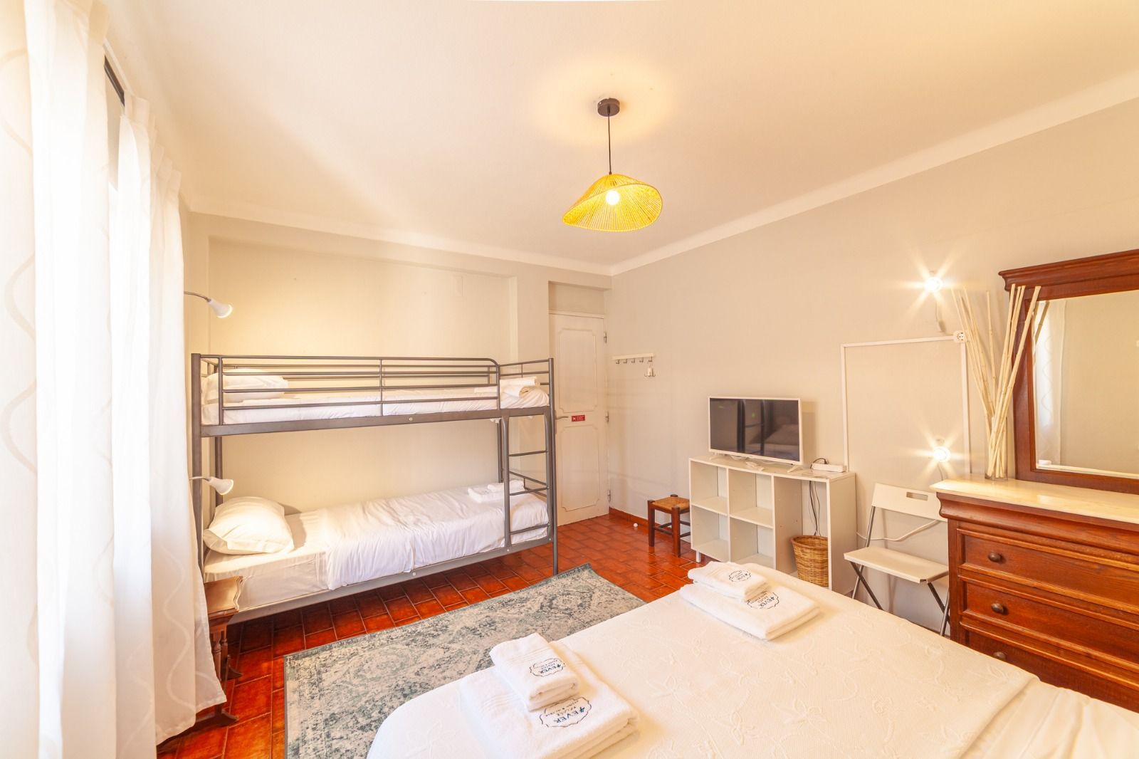 Bright bedroom with bunk bed, single bed, dresser, and TV on a stand