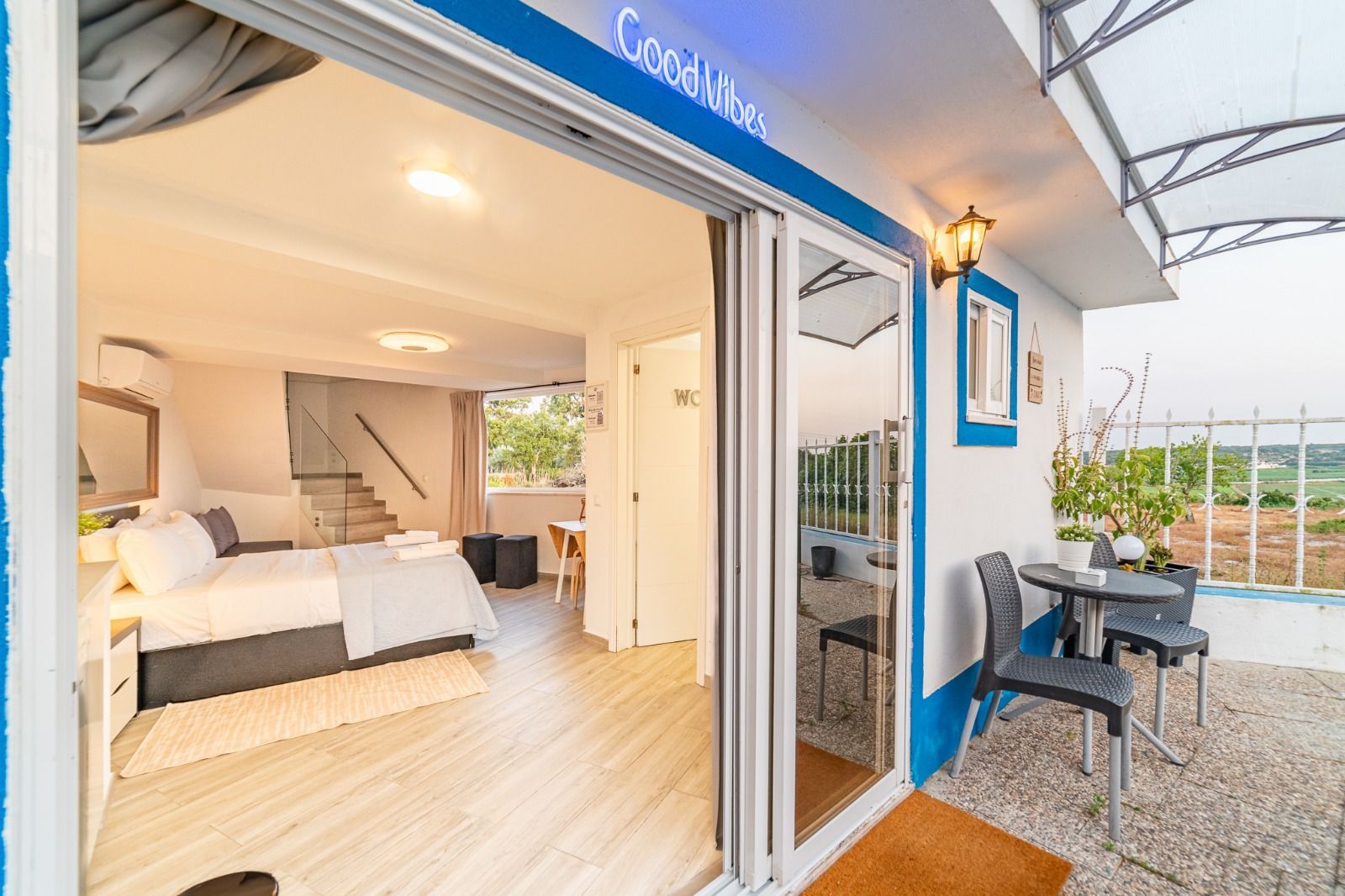 Open sliding doors to a bright bedroom and patio with wicker chairs and table.