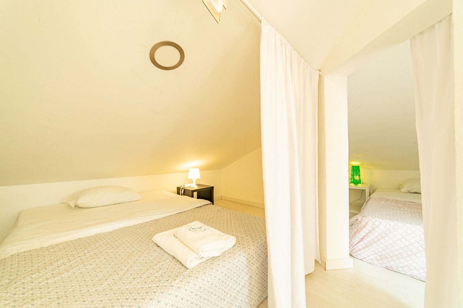 Bright attic bedroom with a bed, bedside lamp, and white curtain divider.