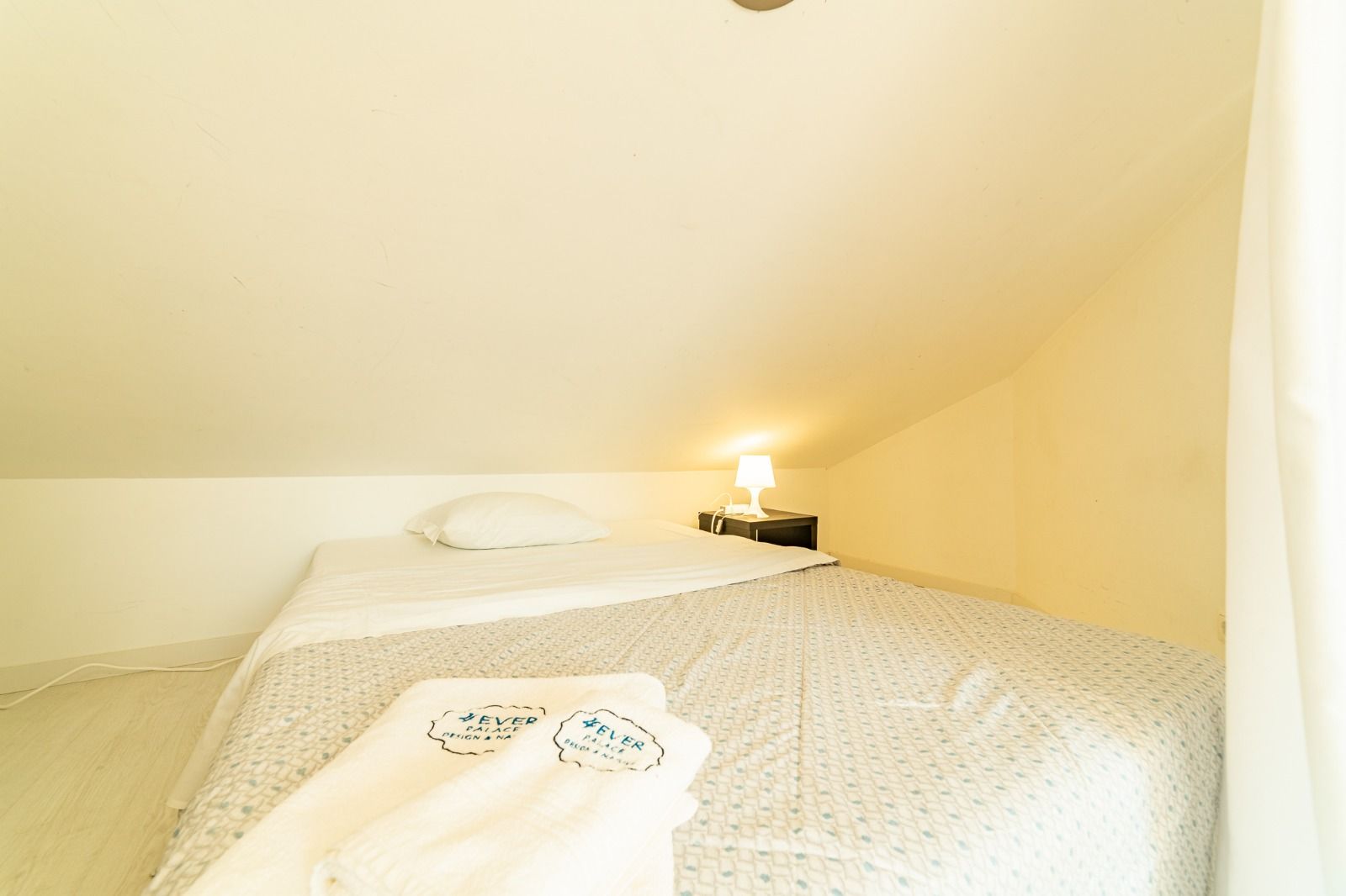 Small attic bedroom with two beds, white bedding, and a warm bedside lamp