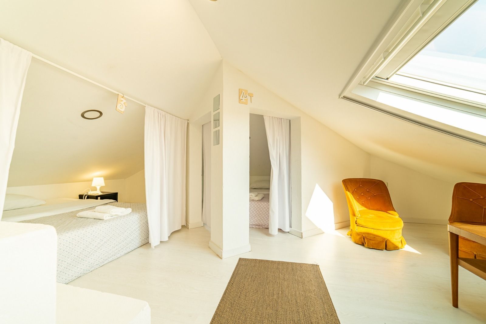 Bright attic bedroom with white curtains, skylights, and yellow chairs in a minimalist interior