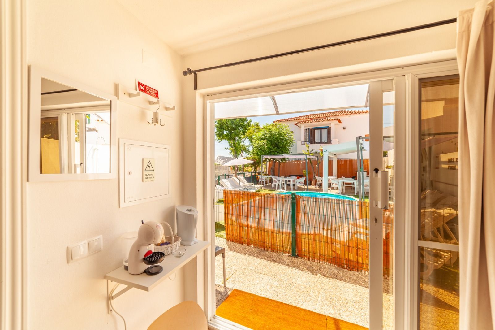 Bright room with open balcony doors, looking out to a sunny patio and orange construction fencing