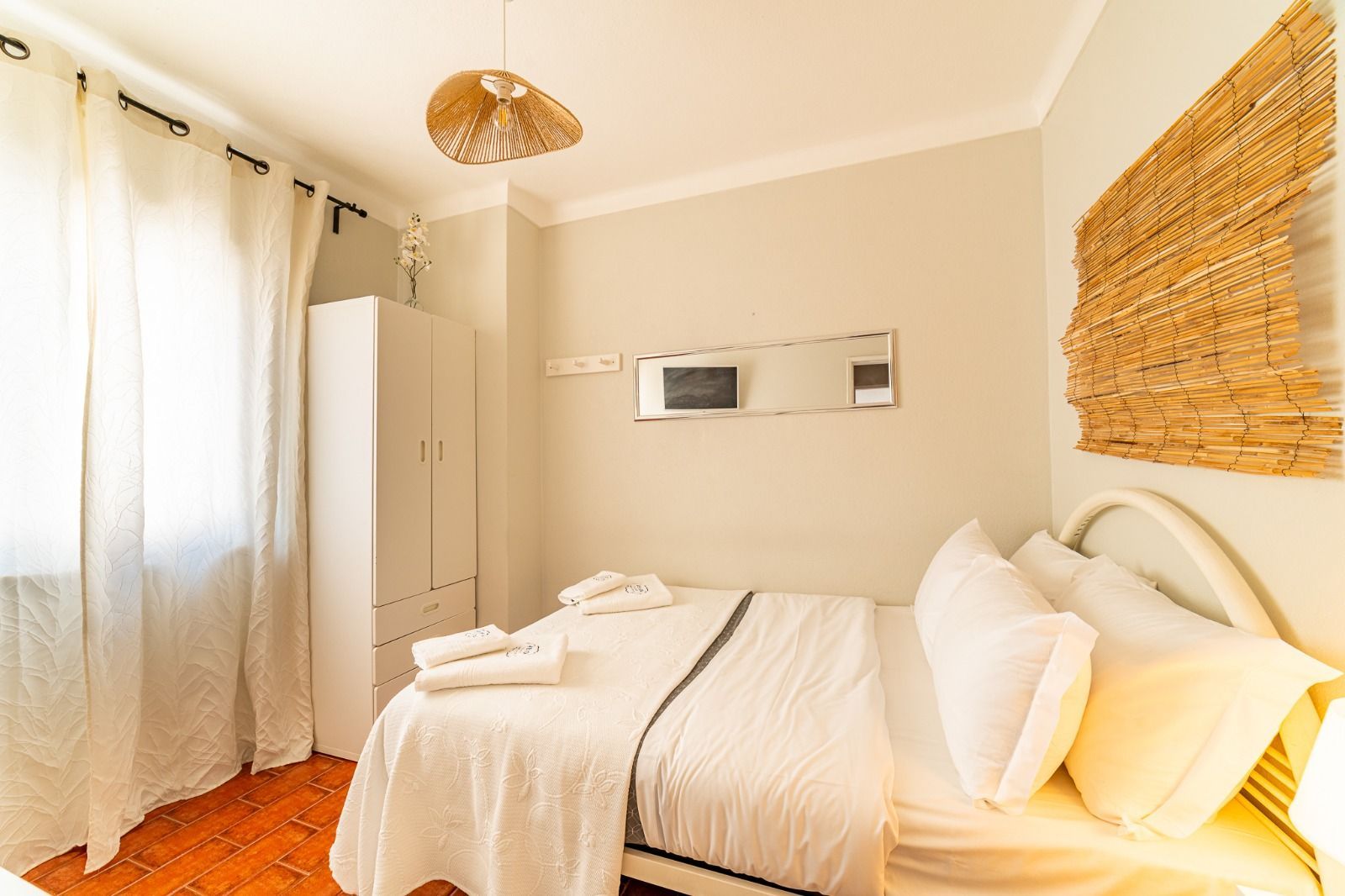 Bright minimalist bedroom with white bedding, sheer curtains, and woven wall decor