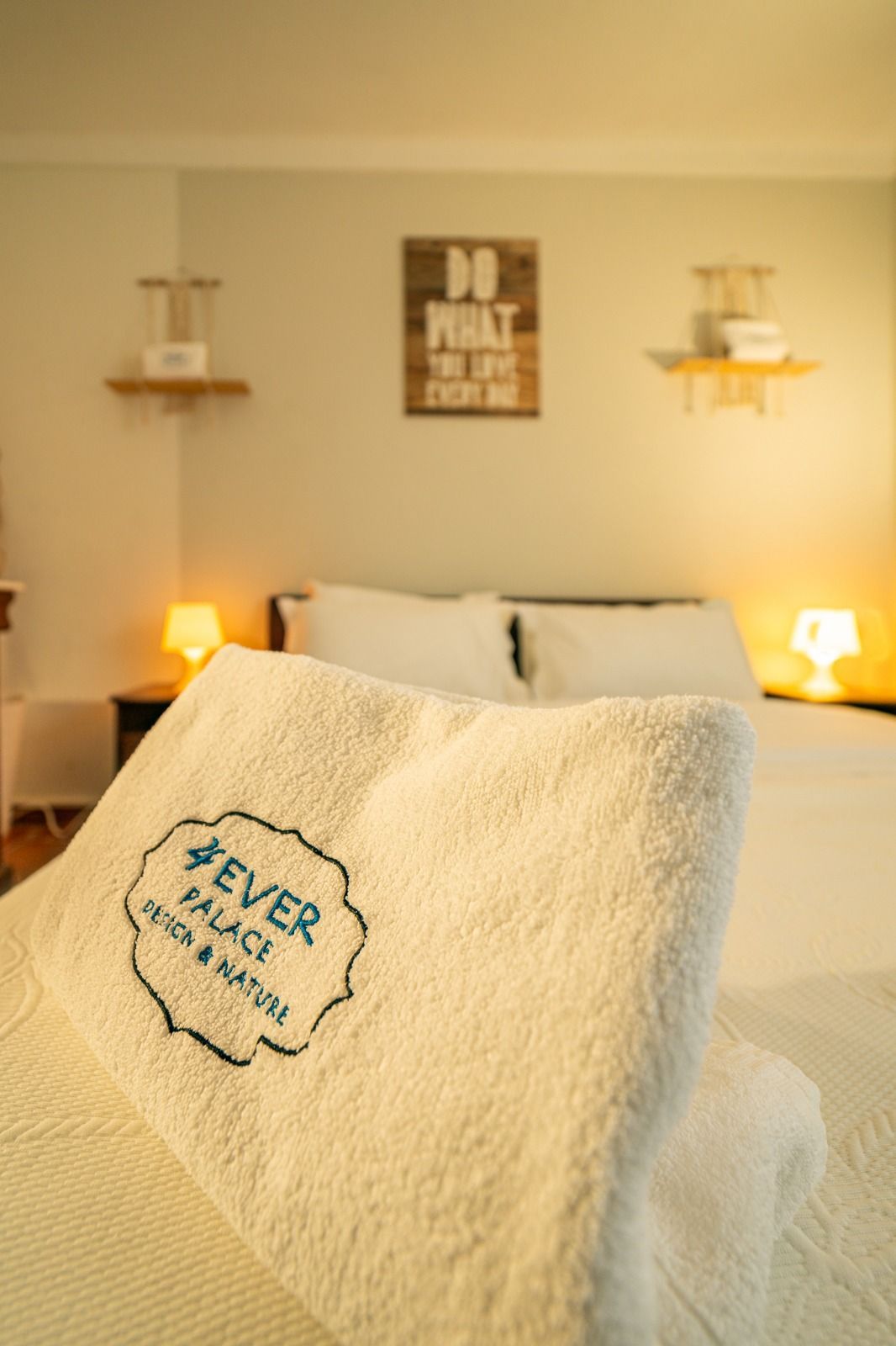 Cozy bedroom with lit bedside lamps and a cream blanket reading “Never Sleep Alone” in the foreground