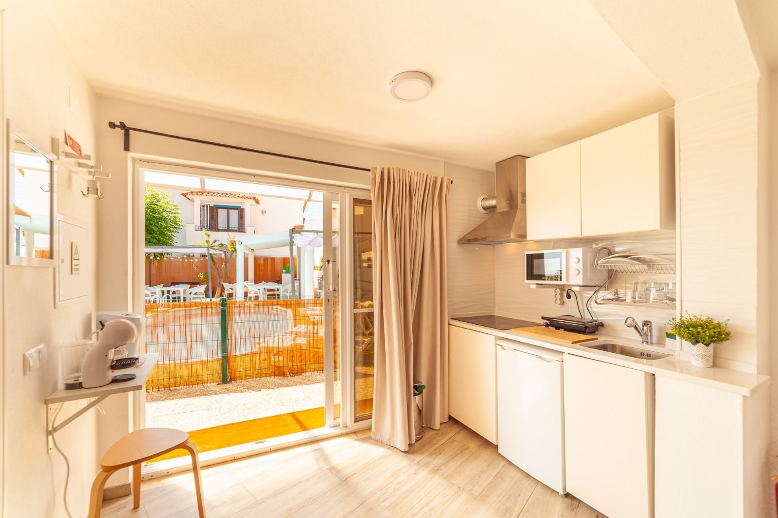 Bright kitchenette opening to a patio through a sliding glass door, with white cabinets and beige curtains.