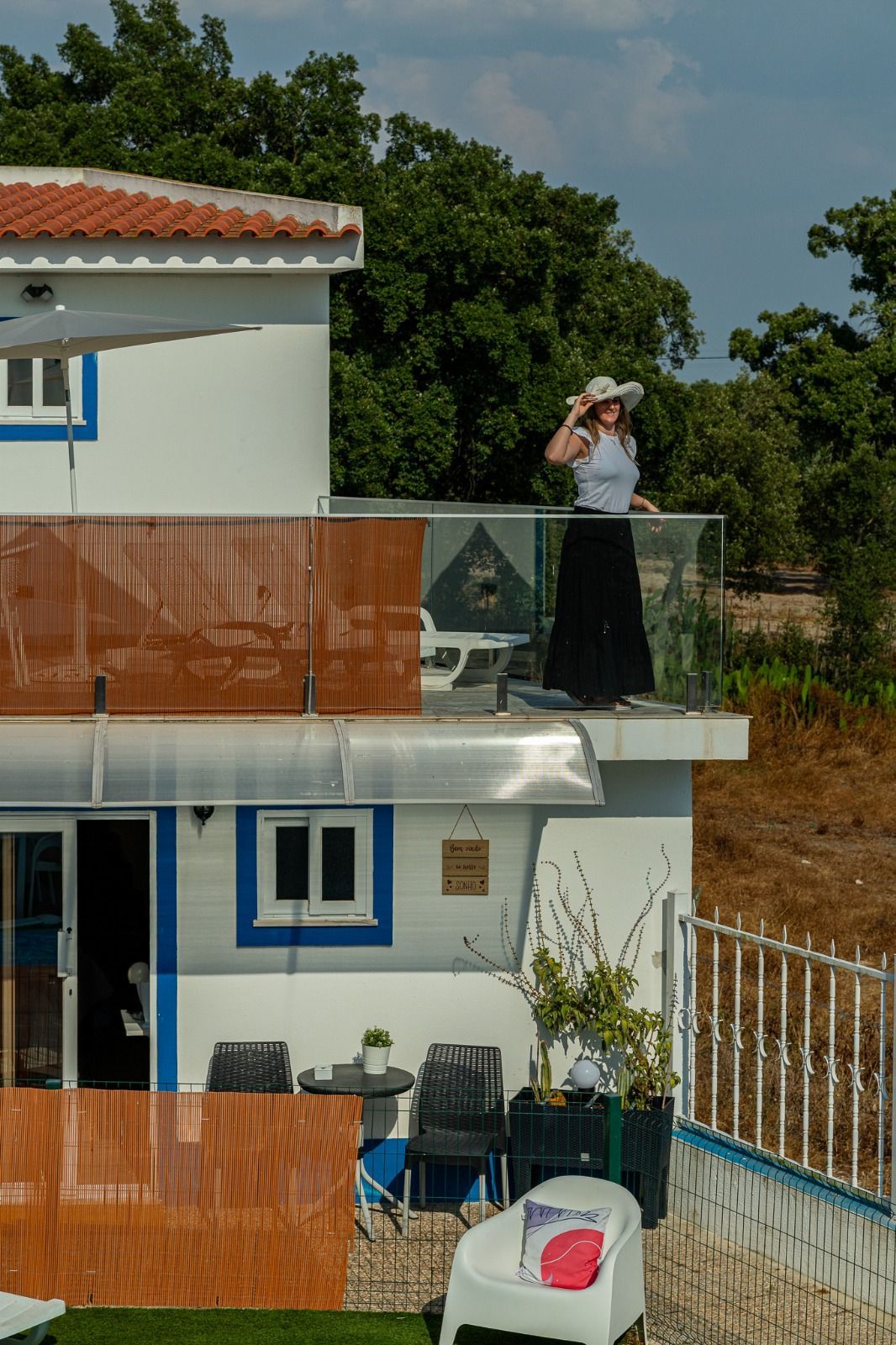 Person standing on a rooftop terrace of a white house with orange railings, holding a camera.