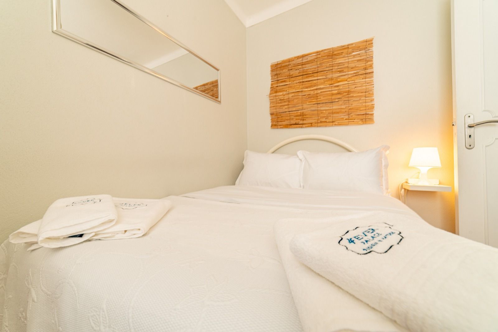Cozy white bedroom with a neatly made bed, wicker wall art, and a lit bedside lamp