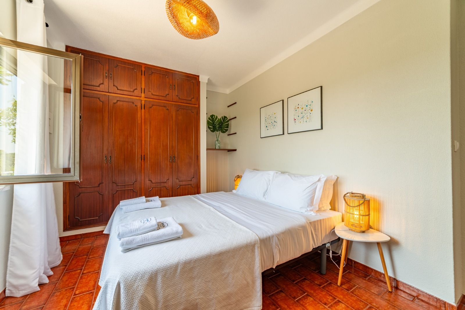 Bright bedroom with white bed, wooden wardrobe, and warm lighting by a window
