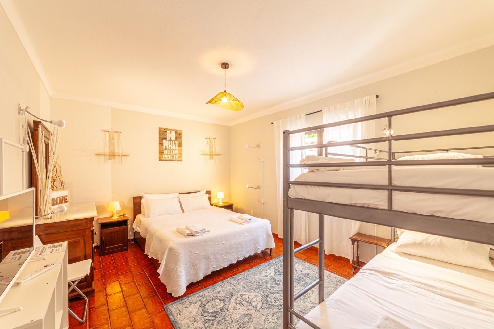 Bright bedroom with a white bed, bunk bed, terracotta floor, and a window with curtains