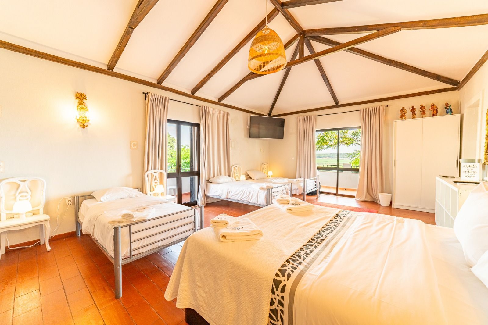 Bright bedroom with two beds, white walls, wooden floor, and large windows with curtains