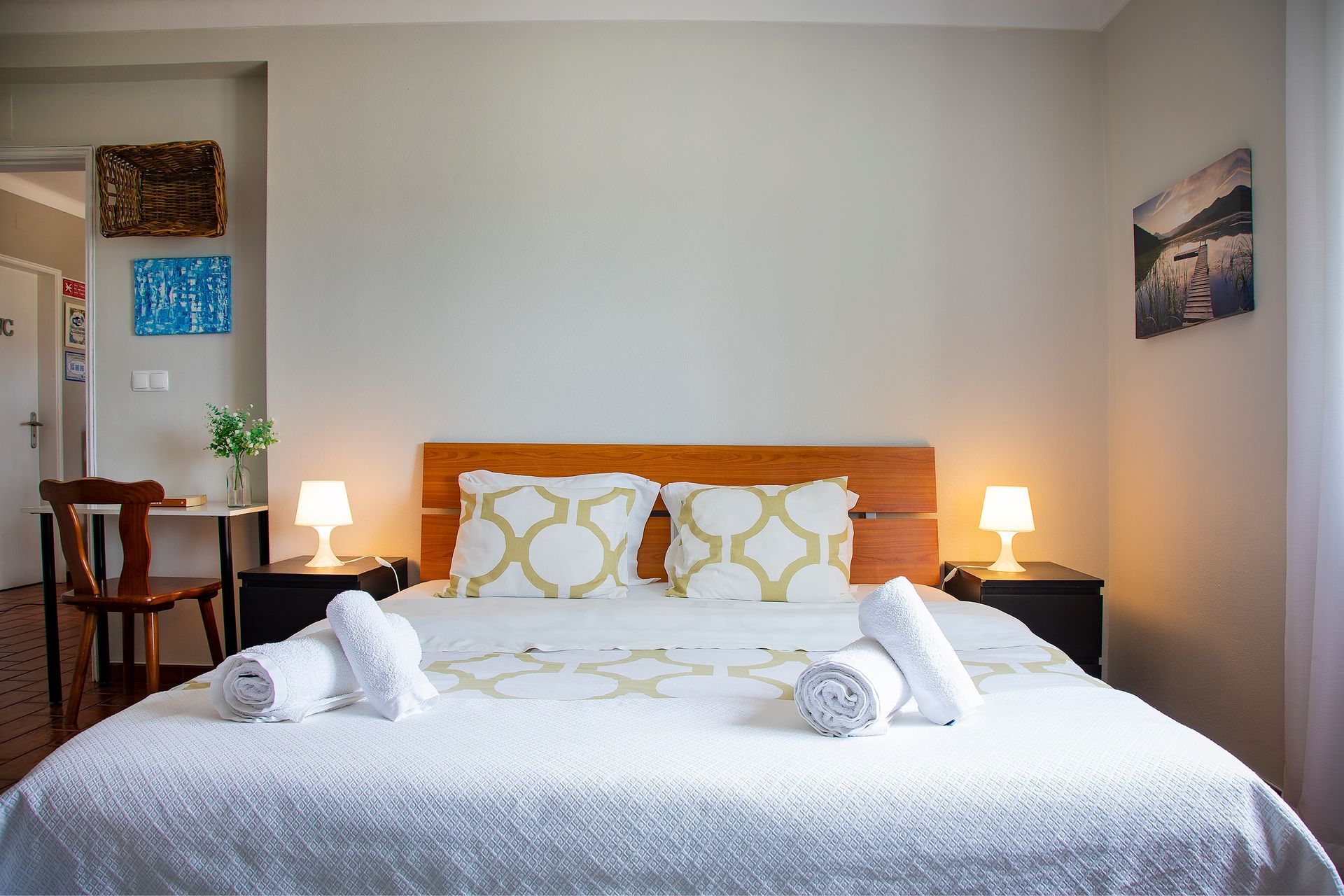 Neatly made bed with white bedding and orange pillows in a softly lit bedroom with bedside lamps.