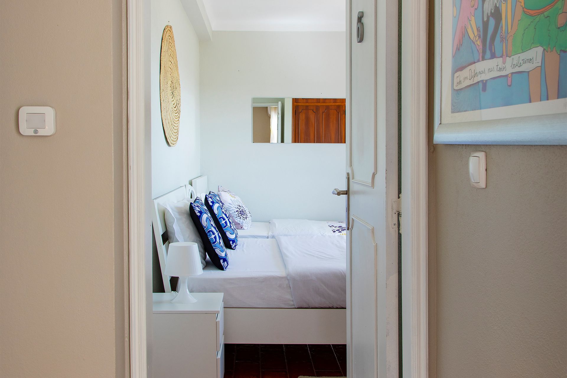 View through doorway into a bright bedroom with a white bed and blue pillows