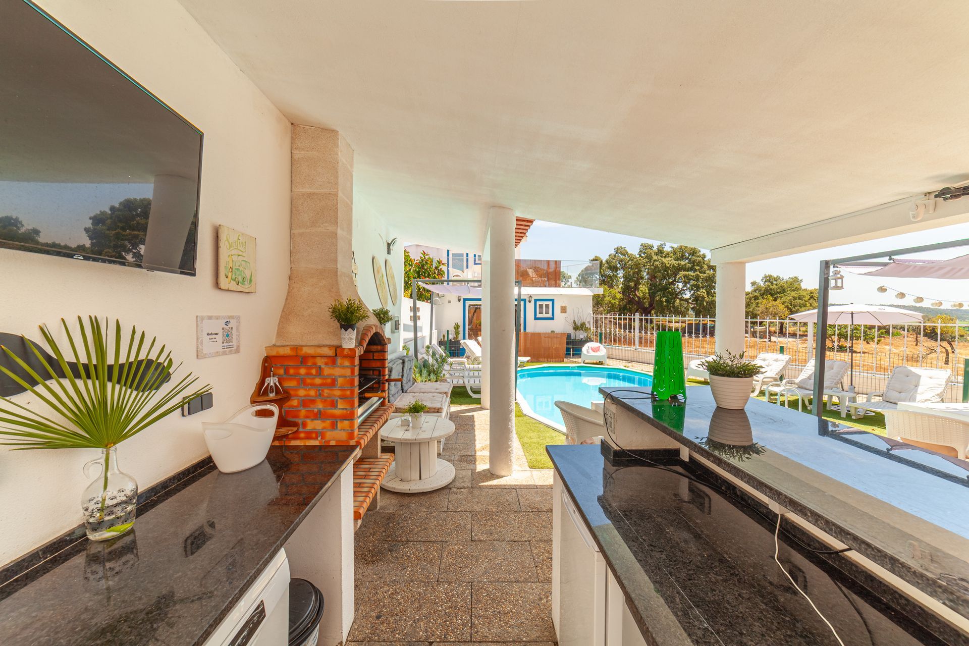 Covered patio with black sofa, brick barbecue, and a view of the pool and garden outside