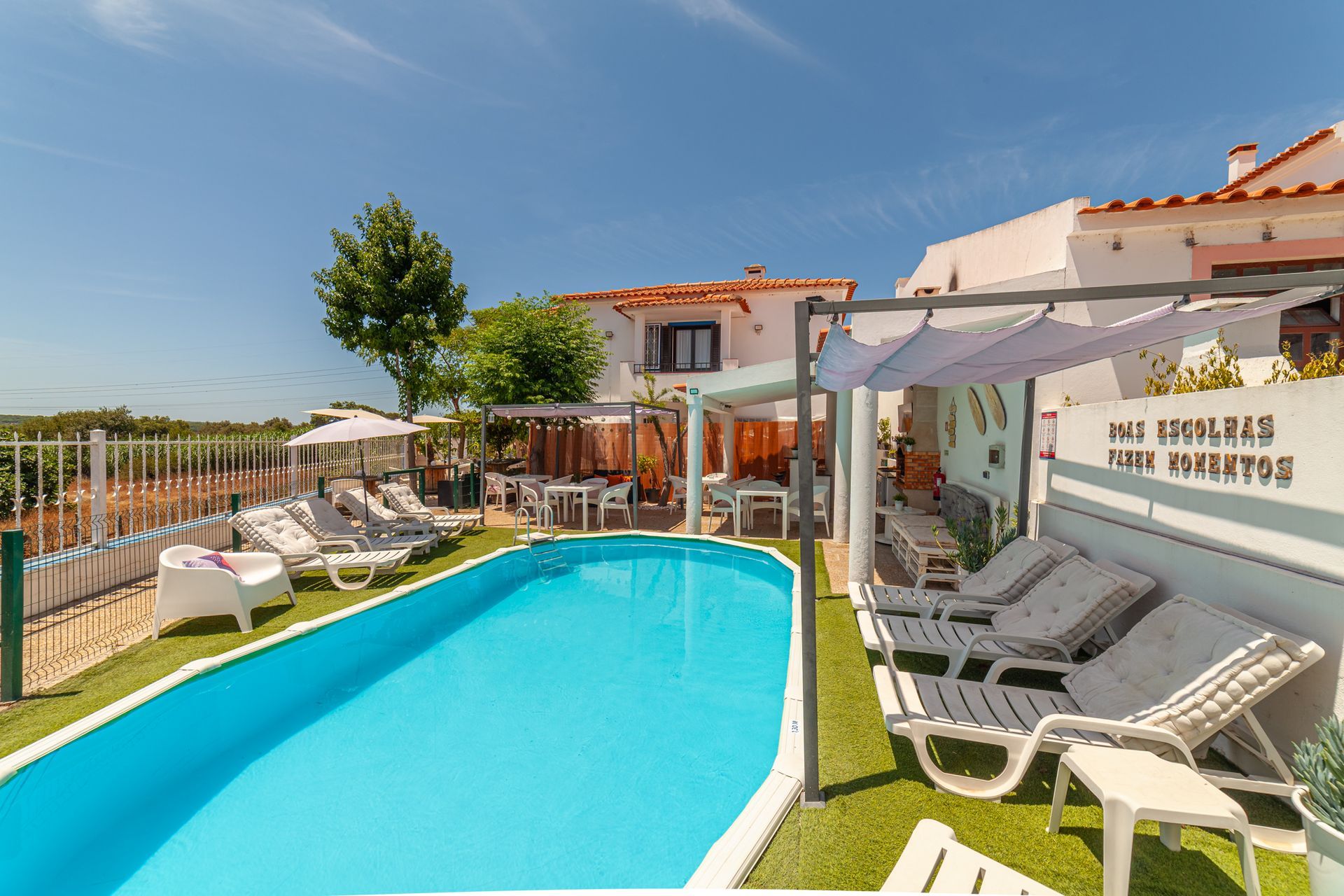 Sunny backyard with a turquoise pool, lounge chairs, and a shaded pergola beside a white house