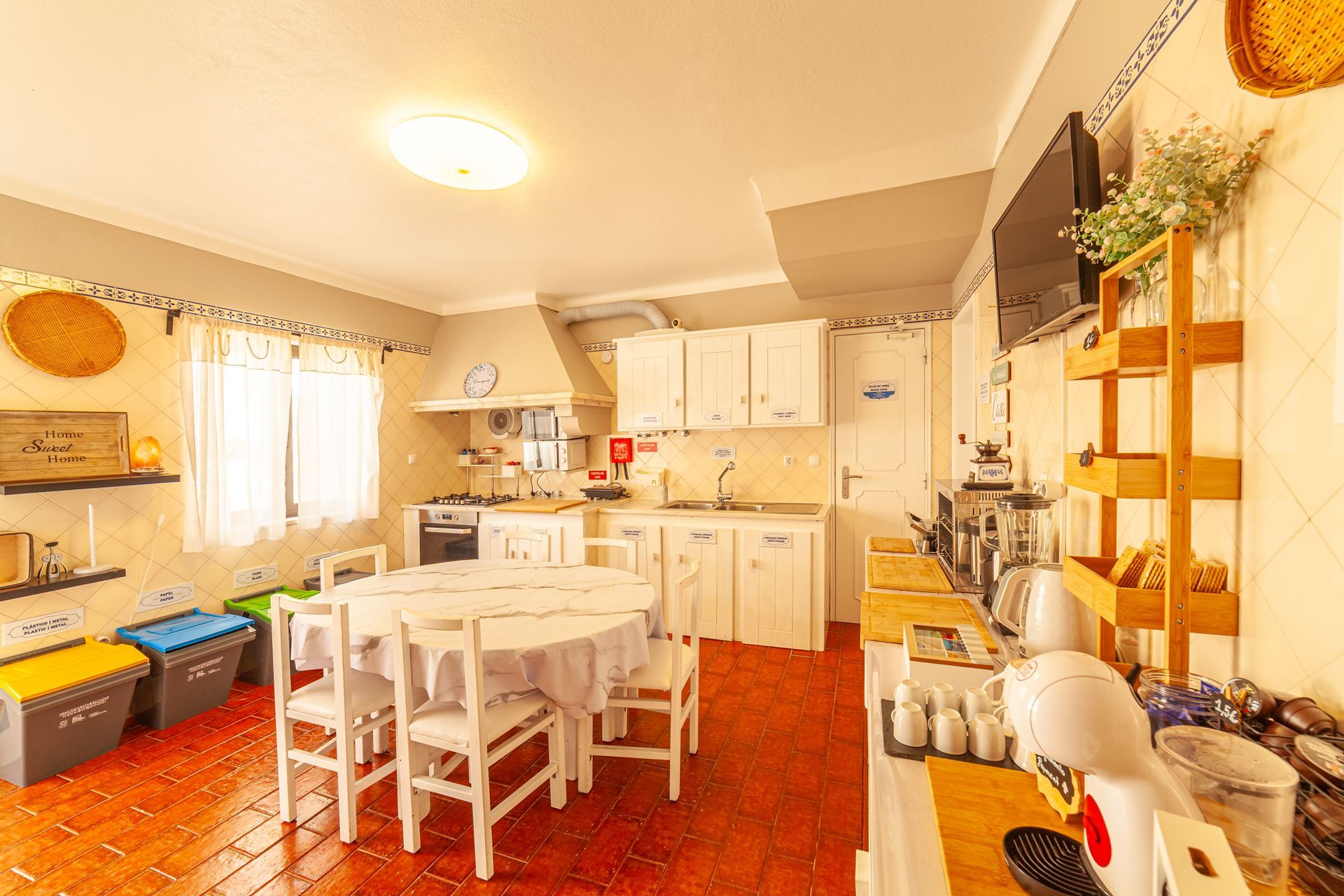 Bright kitchen-dining room with white cabinets, a table and chairs, and warm red flooring.