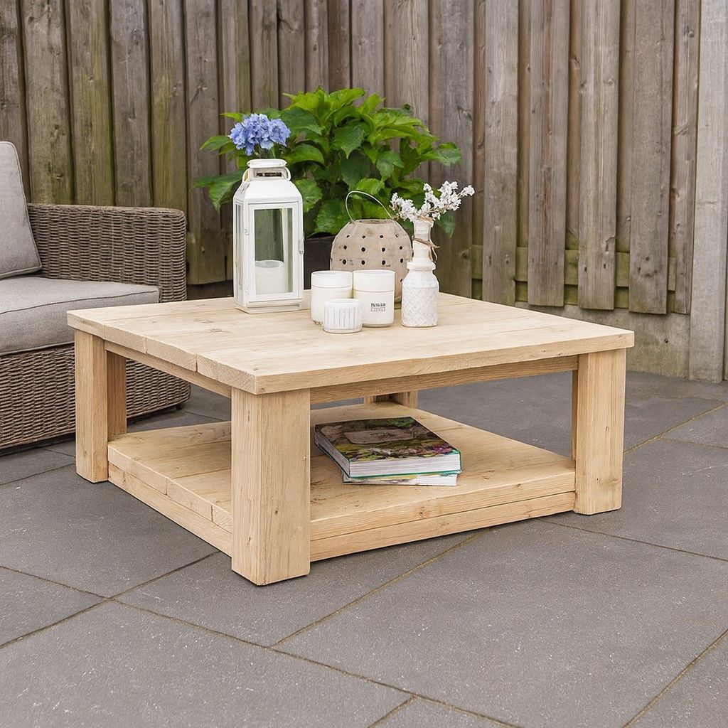 Houten salontafel voor buiten met lantaarn, bloemen en decoratie op een terras tegen een schutting.