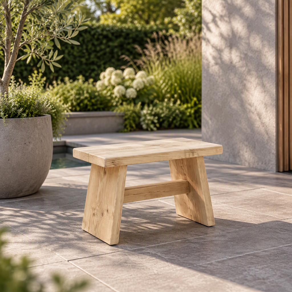 Klein rustiek steigerhouten krukje op een stenen terras met planten op de achtergrond