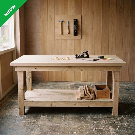 Houten werkbank in een werkplaats met gereedschap aan de muur en houten onderdelen eronder opgeborgen.