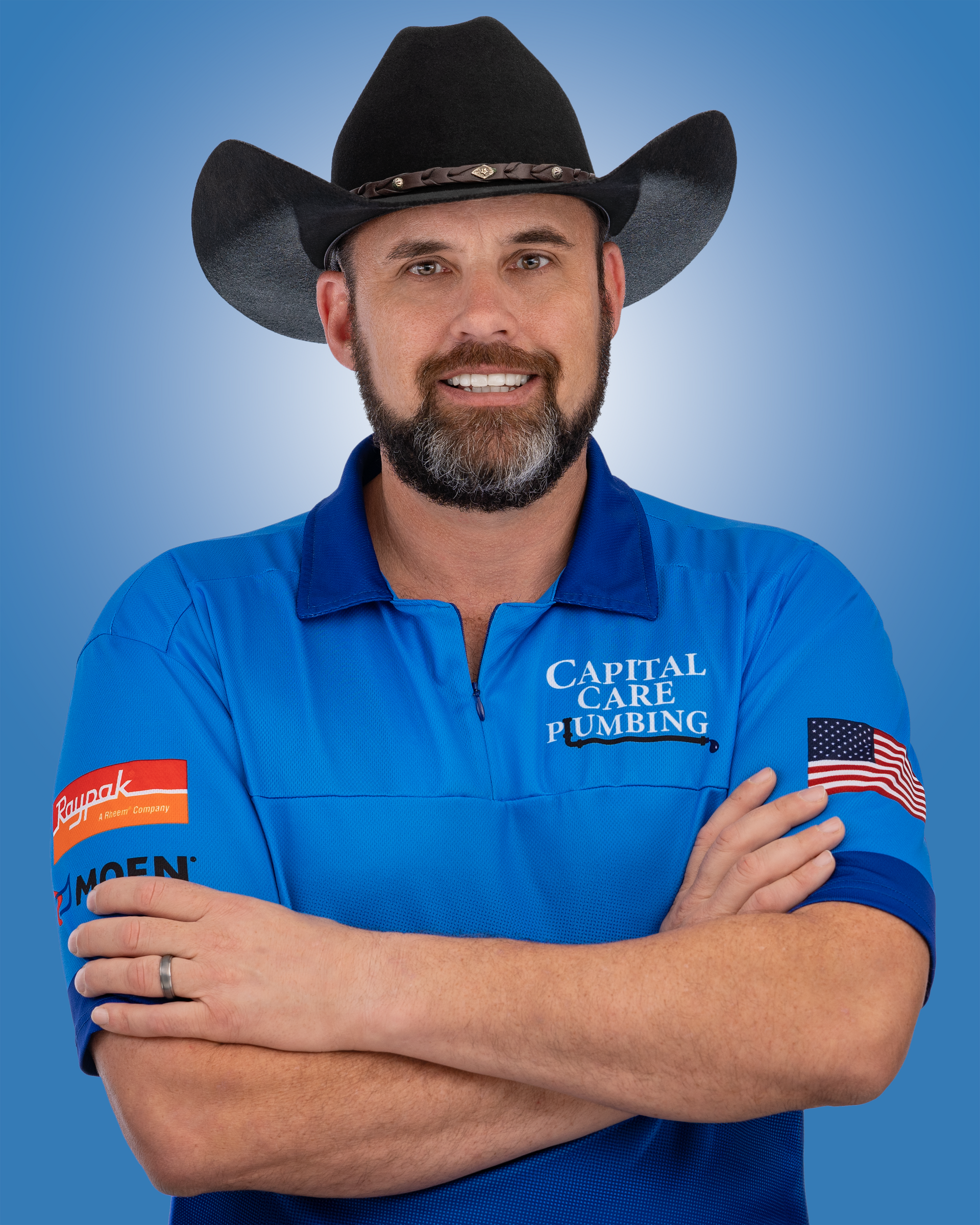 A man wearing a cowboy hat and a blue shirt is standing with his arms crossed.