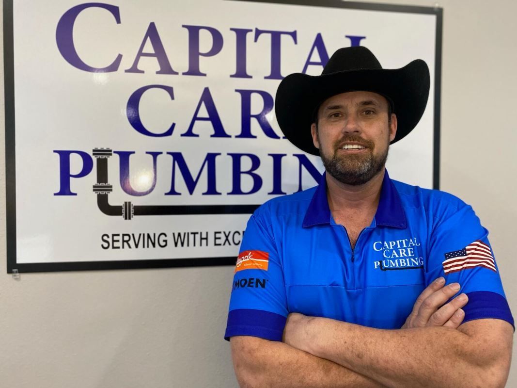 A man wearing a cowboy hat is standing in front of a sign for capital car plumbing.