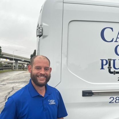 A man in a blue shirt is standing in front of a plumbing company van