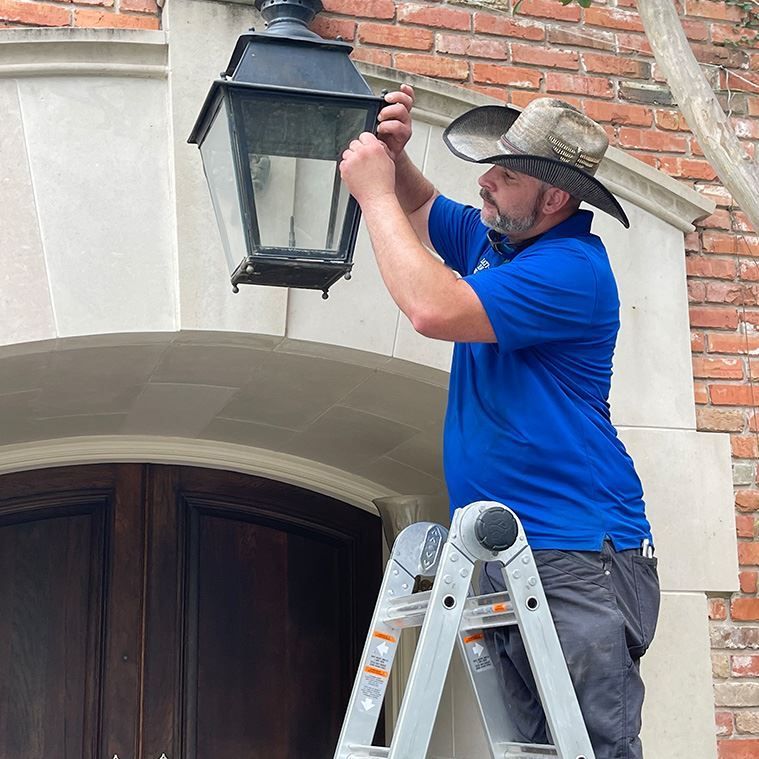 A man in a cowboy hat is standing on a ladder fixing a lantern.