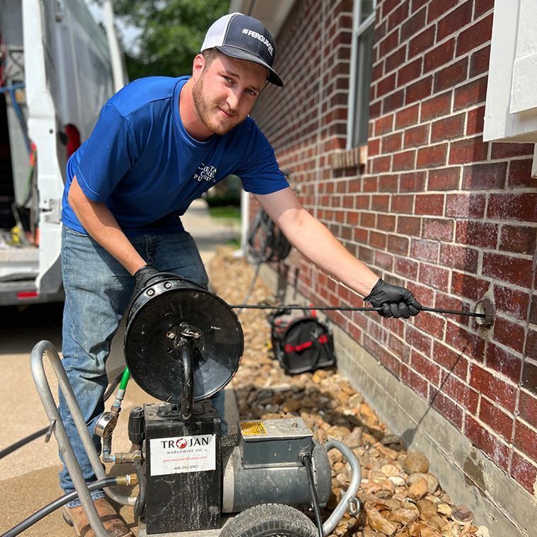 A man is using a machine to clean a drain on the side of a brick building.