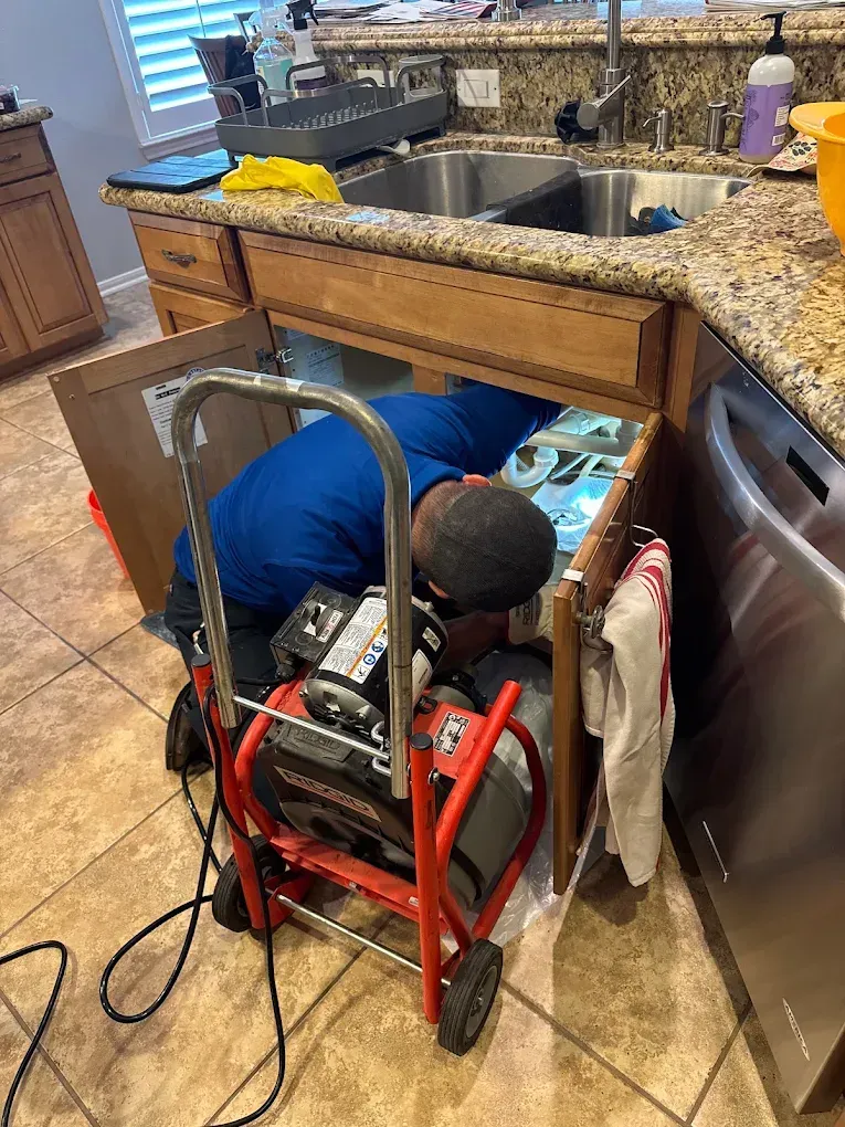 Plumber clearing a clogged kitchen sink drain with professional equipment.