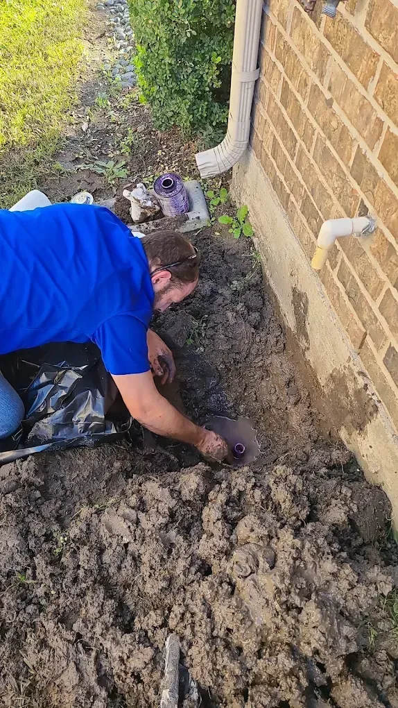 Plumber repairing a buried sewer line in a trench outside a residential home