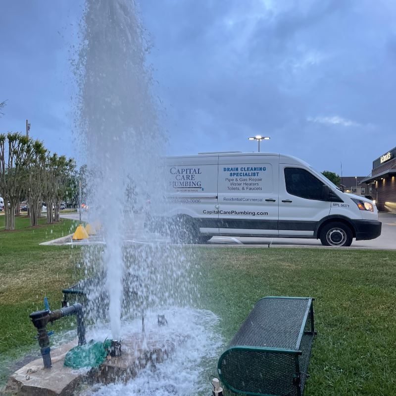 A white van is parked next to a fountain in a park.