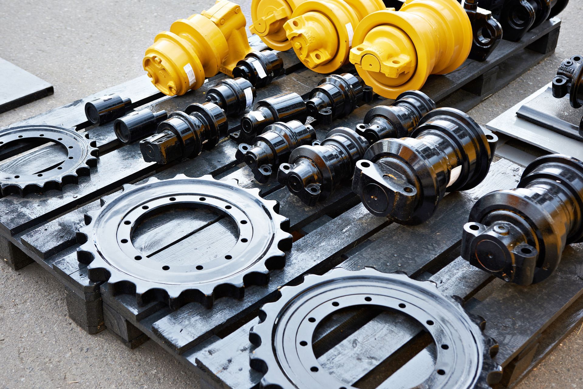Heavy machinery parts, including sprockets and rollers, arranged on a pallet.