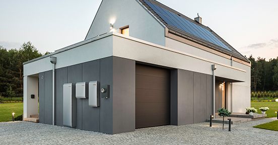 Modern gray house exterior with sloped roof, solar panels, and garage on a gravel driveway