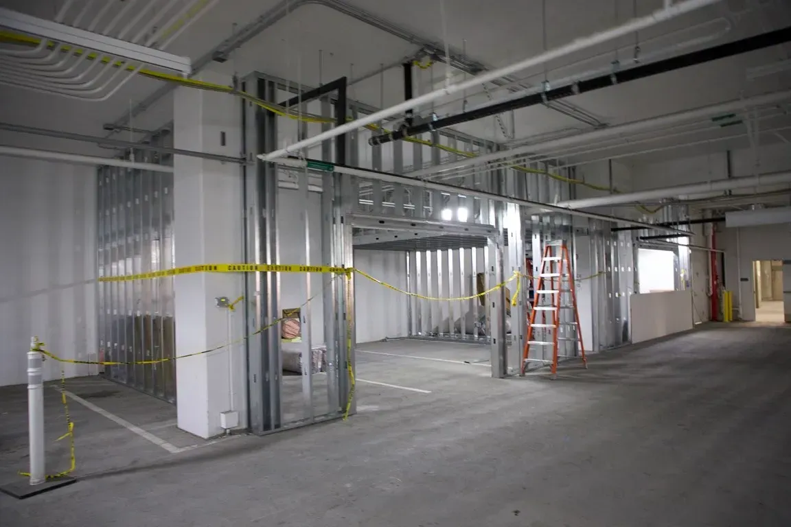 Empty unfinished interior with concrete floor, metal framing, ladders, and caution tape in a construction area