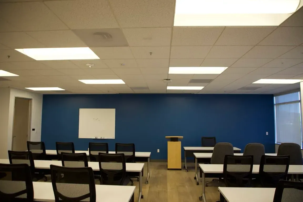Empty classroom with rows of chairs facing a podium and blue front wall