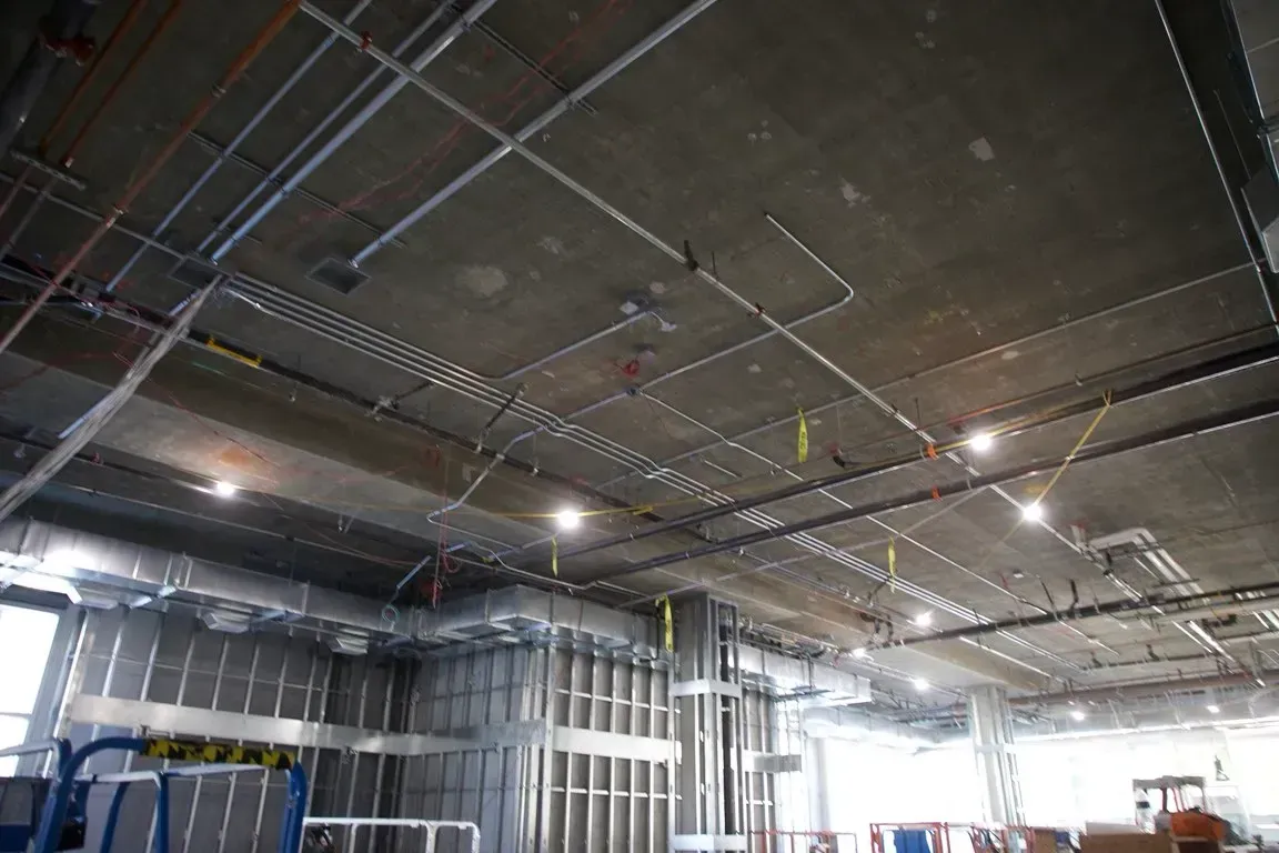 Interior construction site with exposed ceiling ducts, pipes, and bright overhead lights