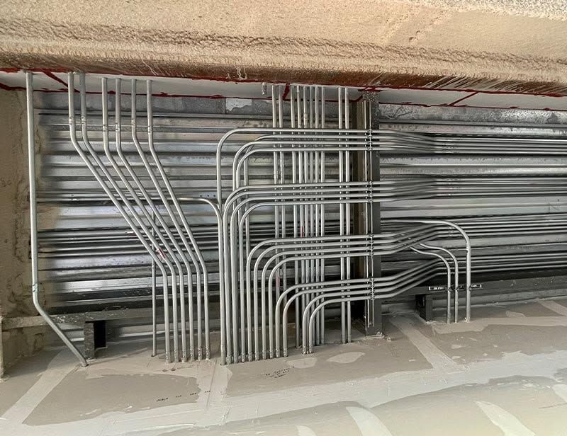 Metal electrical conduits routed in a wall cavity with exposed wiring and unfinished plaster around them