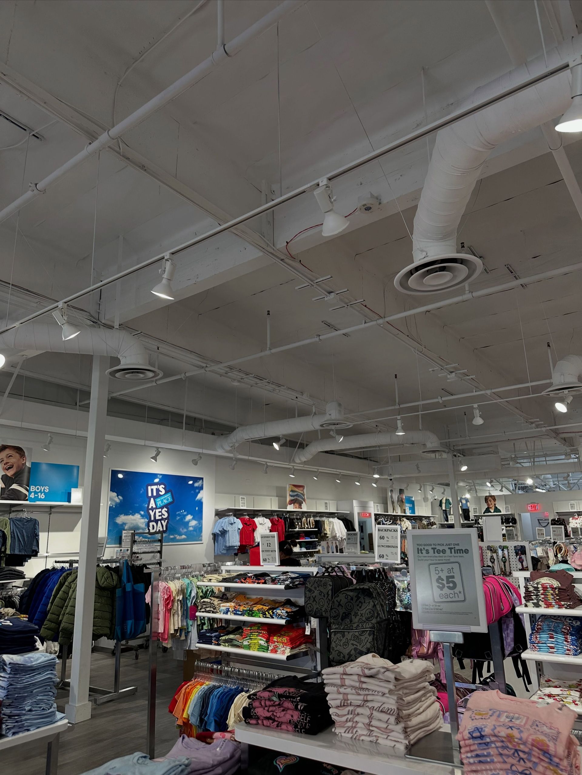 Clothing store interior with racks of folded clothes, hanging apparel, and exposed white ceiling ducts
