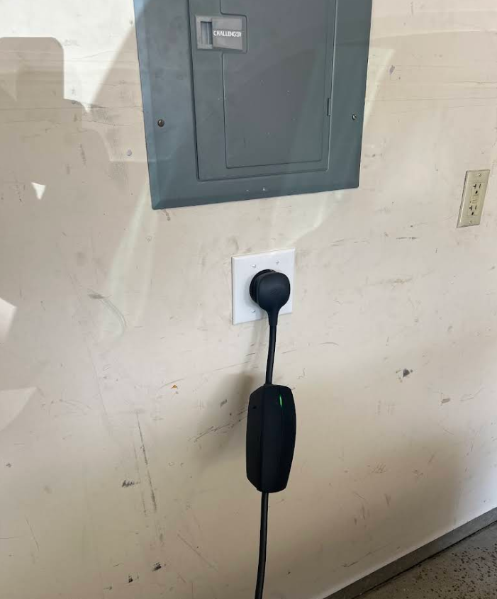 Wall with electrical panel and outlet; a black plug-in device hangs from the outlet near the floor.
