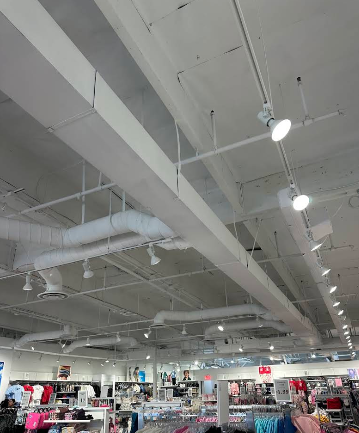 Retail store interior with white ceiling beams, track lights, and clothing racks below