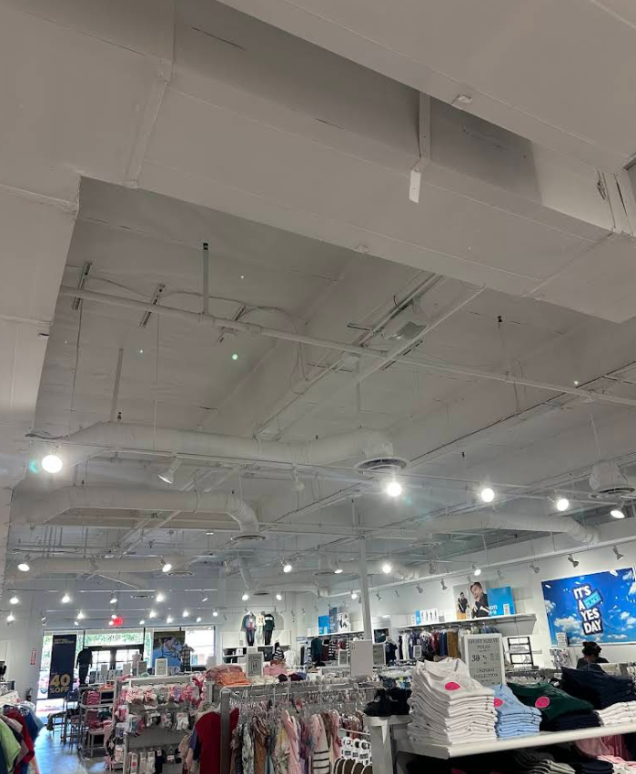 Clothing store interior with white ceiling beams, hanging lights, and racks of folded clothes and garments