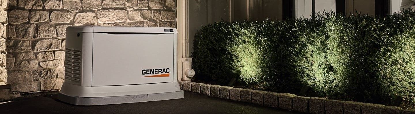 Commercial HVAC unit beside a stone wall and neatly trimmed hedges at night