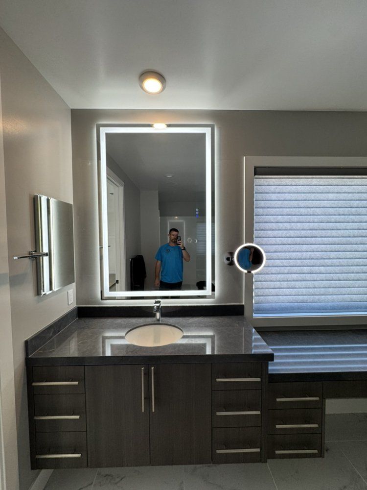 Modern bathroom vanity with large mirror, dark wood cabinets, sink, and window blinds; person reflected in mirror
