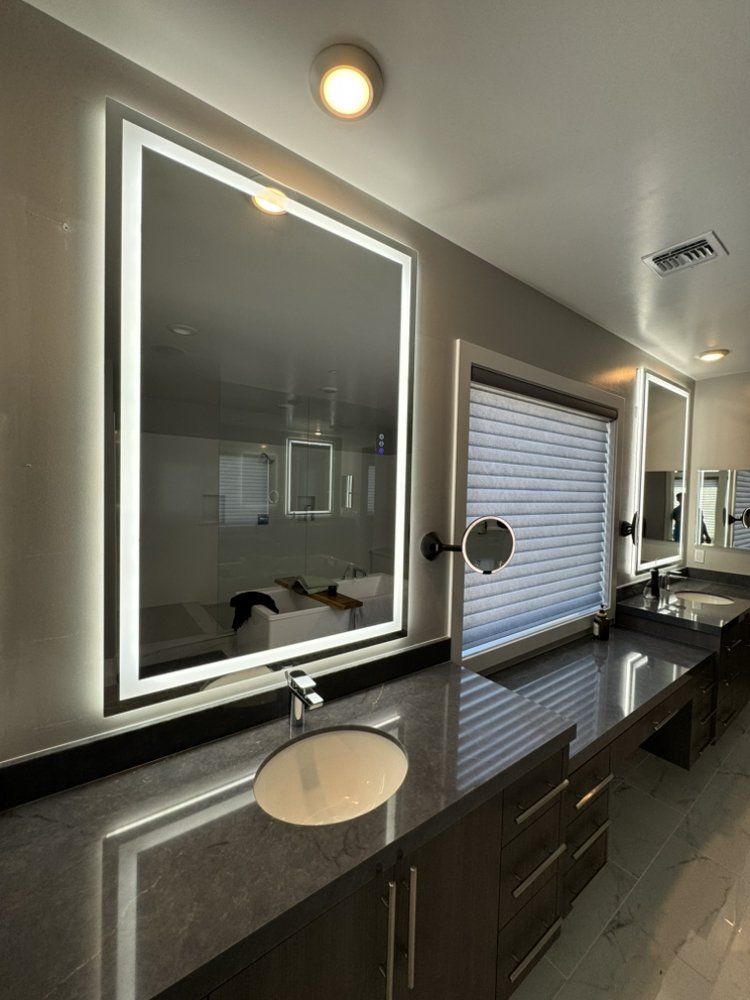 Modern bathroom vanity with illuminated mirror, sink, dark countertop, and window blinds