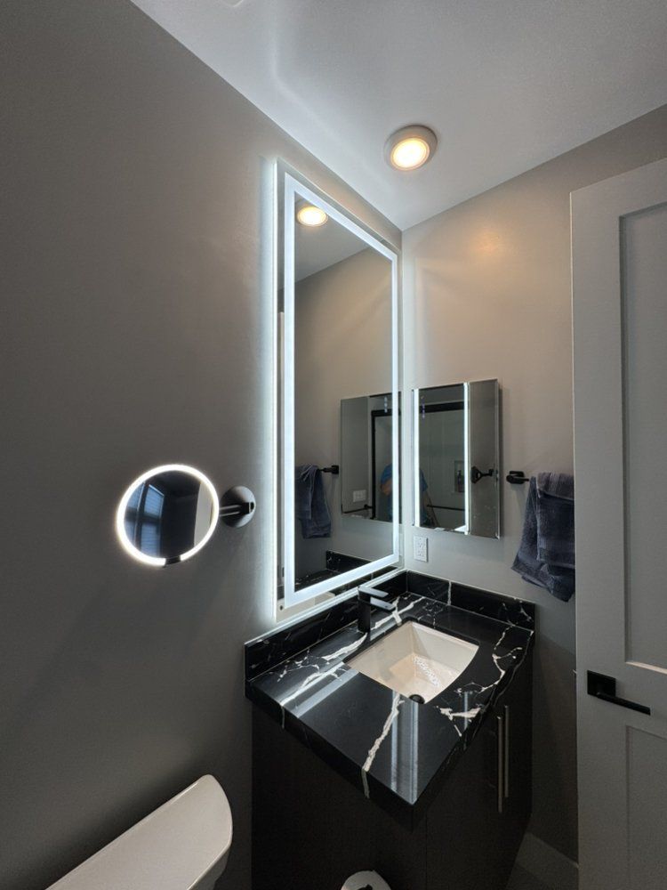 Modern bathroom with lit mirror, black vanity, and sink beside a towel rack