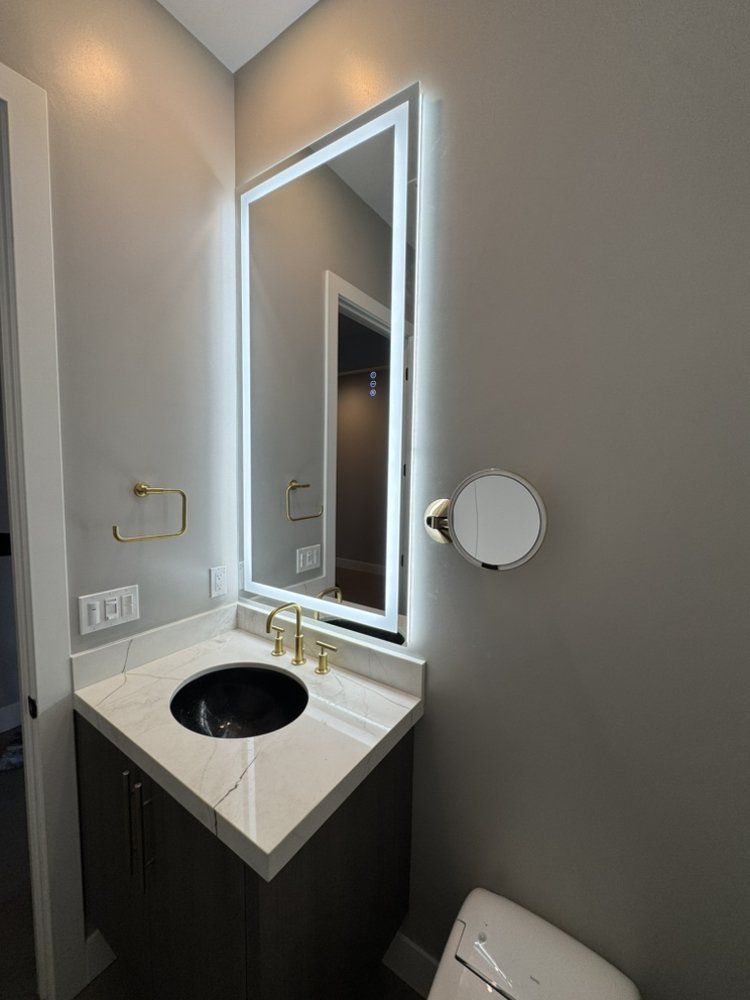 Small modern bathroom vanity with white countertop, black cabinet, oval sink, mirror, and wall-mounted toilet paper holder.