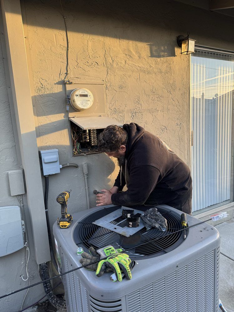 Technician repairing an outdoor HVAC unit beside a house, with tools on top.