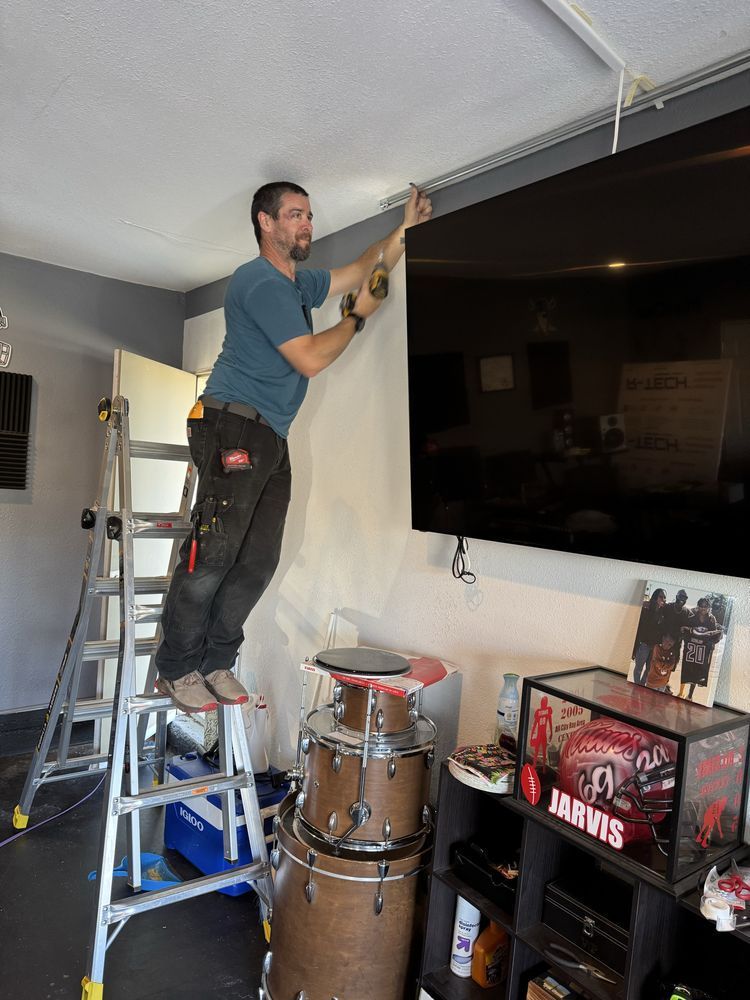 Man painting a wall beside a large TV in a living room on a ladder
