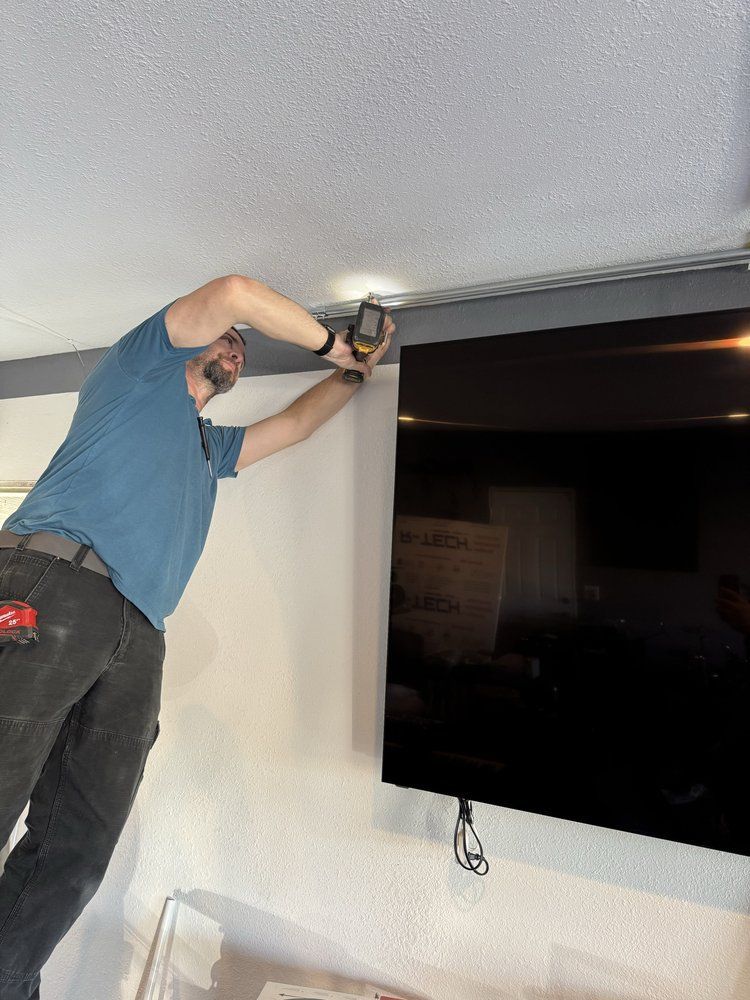 Person drilling into the wall above a mounted TV in a room