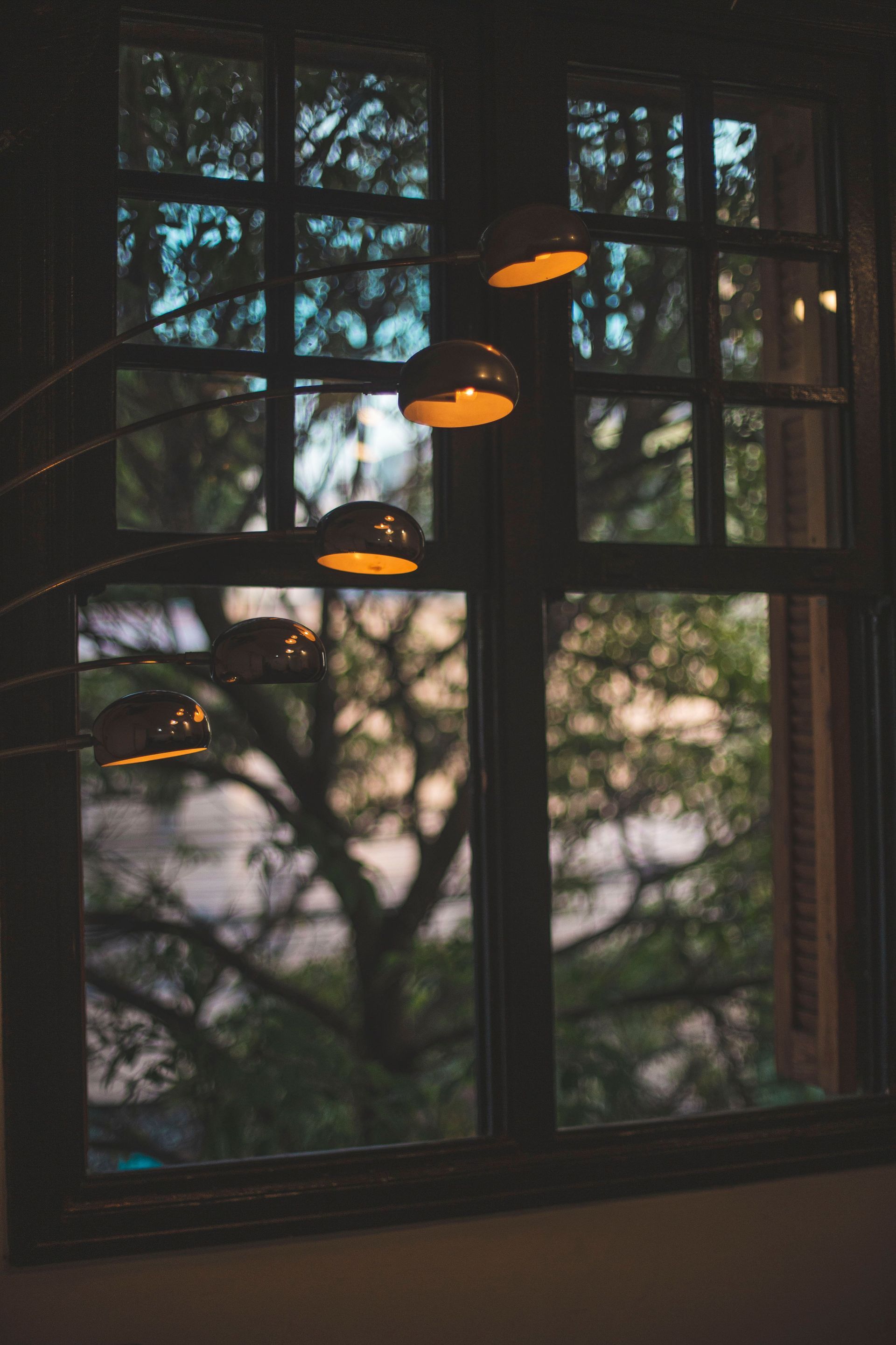 Hanging pendant lights reflected in a window, with trees visible outside at dusk