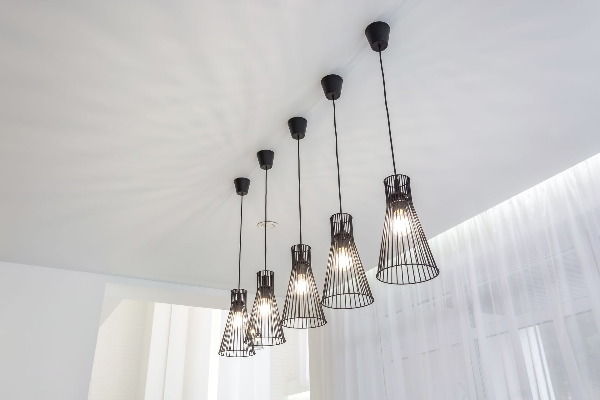 Five black pendant lights hanging from a white ceiling in a bright room